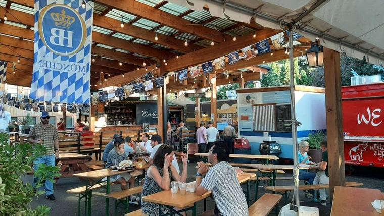 Diners at picnic benches under a covered Portland food cart pod