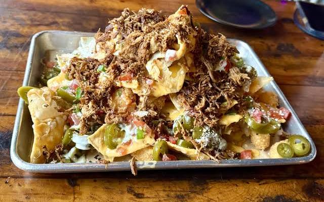 Shredded carnitas piled over nachos on a metal tray