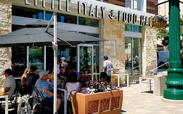 Diners at outdoor tables in front of the Little Italy Food Hall